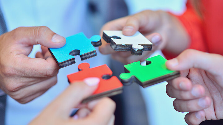 Grafika dekoracyjna, cztery dłonie skierowane ku sobie składają puzzle